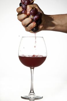Hand is squeezing grapes to make juice over a glass of red wine