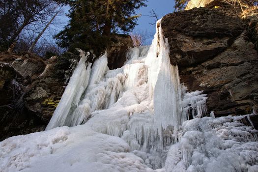 View of the frozen waterfall with trees and rocks and blue sky