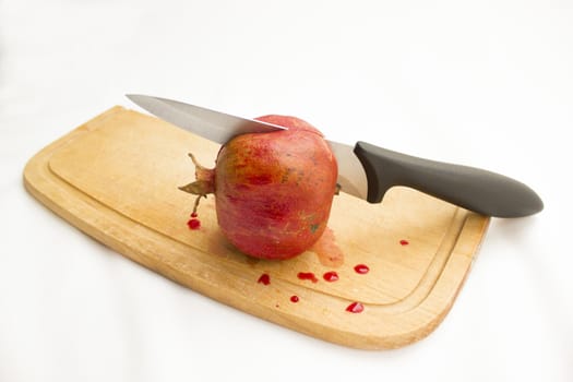 Pomegranate on a wooden cutting board with a knife inside.