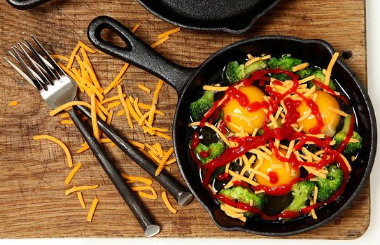 Uncooked Raw Eggs in Skillet with Brocolli, Cheese and Sriracha Sauce ready to put in oven.