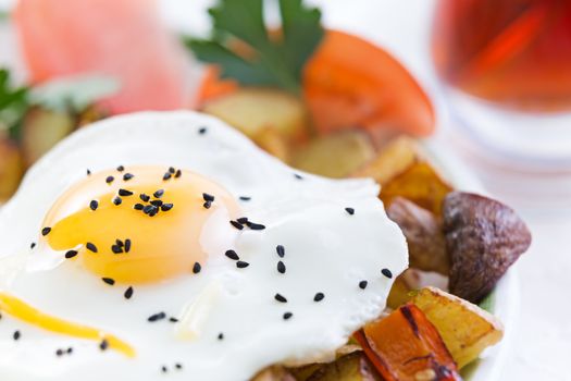 Nutritious fried egg served sunny side up with healthy fresh vegetables including diced potatoes and mushrooms with tomato garnished with fresh parsley