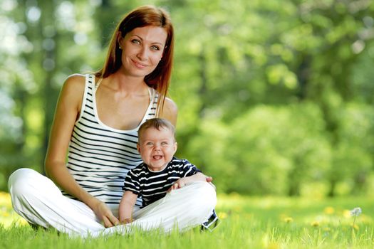 Beautiful young mother and daughter sitting on grass in park