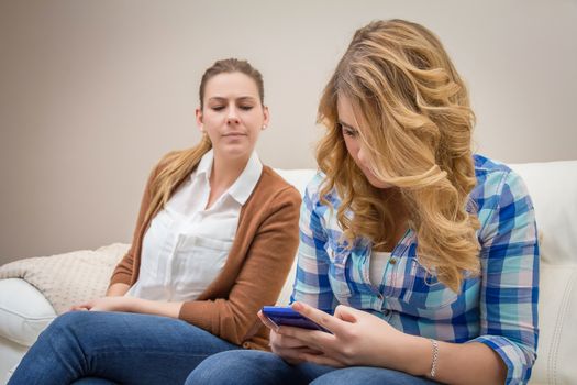 Suspicious mother spying her teenage daughter while looking messages in a smartphone. Bad family communication concept by new technologies