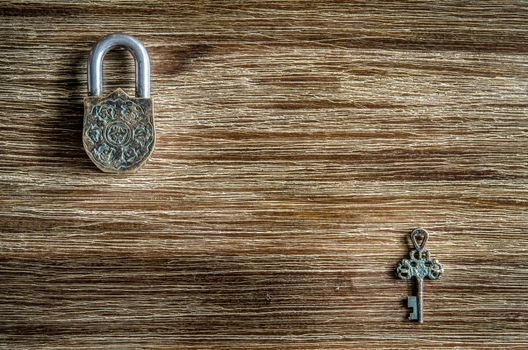 Closed vintage padlock and old key on a wooden texture