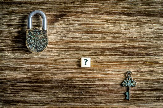 Old vintage padlock and key with question mark on wooden texture