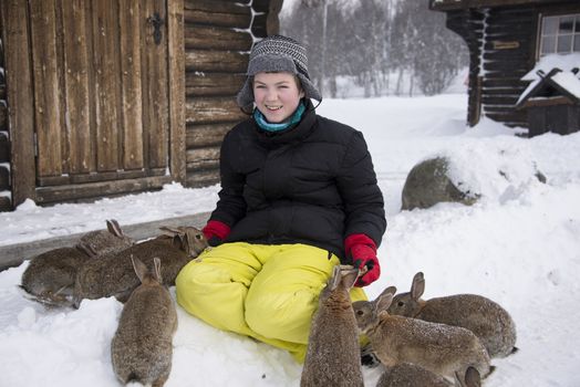 A boy is feeding the rabbits outside on a farm in winter. With snowflakes visible 