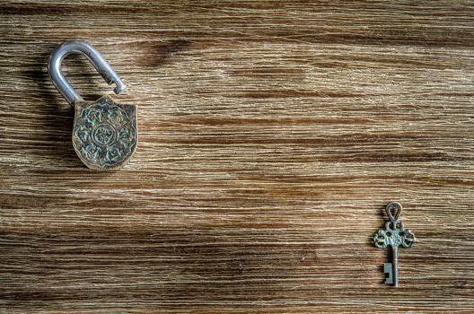 Open vintage padlock and old key on a wooden texture