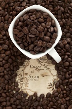 Cup full of coffee beans on the old map