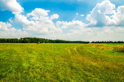 Yellow helicopter on green field by the forest