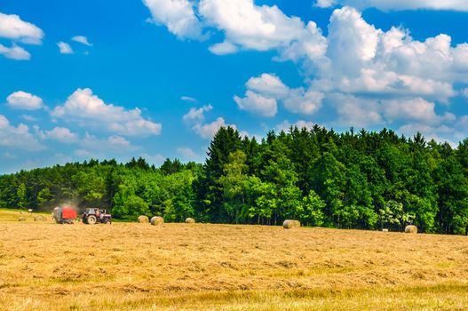 Tractor working in field among the haystacks