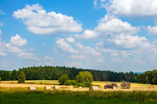 Harvesting time: Tractor working in field among the haystacks