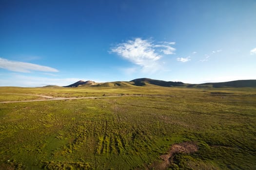 A green plains with mountain landscape in the background against a blue sky at Tibetan Plateau