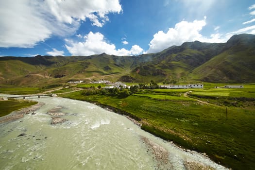 A rural Tibetan settlement by the river. Mountain landscape on the background with cloudy blue sky.