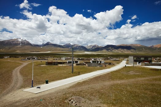 A Tibetan rural village in the outskirts. Snow capped mountain landscape with cloudy sky