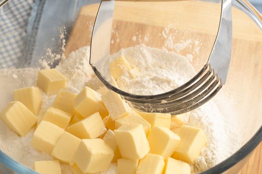 Butter in bowl with flour and handheld pastry blender.