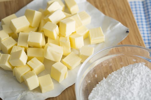 Fresh butter cubes on cutting board with bowl of flour.
