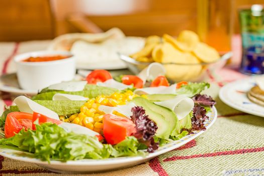 Traditional mexican food in a table, with bowl of nachos, spicy sauce, tortillas and fresh salad