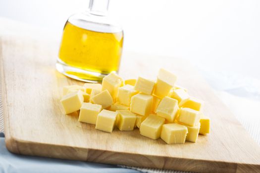 Butter pieces (cubes) on a cutting board, with bottle of vegetable oil in the background