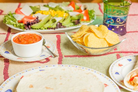 Traditional mexican food in a table, with bowl of nachos, spicy sauce, chicken fajita, tortillas and fresh salad
