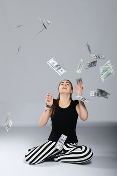 Long-haired teenager girl in striped trousers sitting on the floor and throws into the air dollars