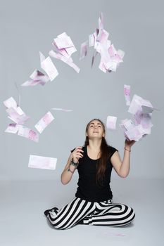 Long-haired teenager girl in striped trousers sitting on the floor and throws into the air euros