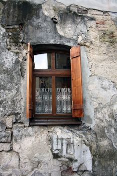 Old window with shutters and curtain on the background of a crumbling wall