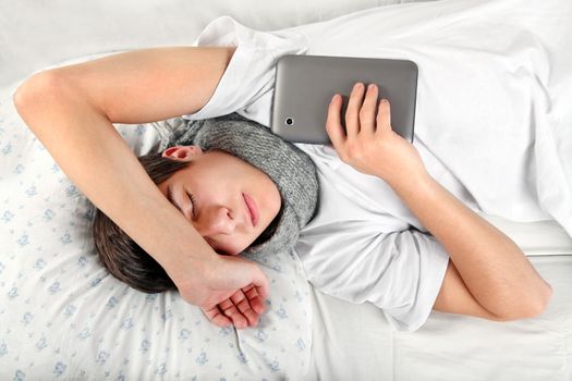 Tired Teenager sleeps with Tablet Computer on the Bed