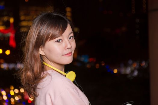Attractive Malaysian female wearing headphones  with city lights in background