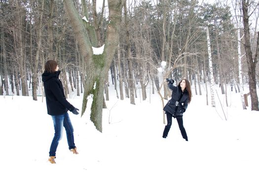 Portrait of happy couple sitting in snowdrift and playing snowballs in winter forest