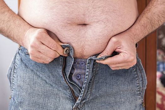 Overweight man trying to fasten too small clothes