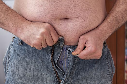 Overweight man trying to fasten too small clothes, fat man with a big belly