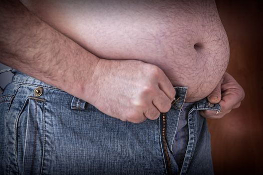 Overweight man trying to fasten too small clothes, fat man with a big belly