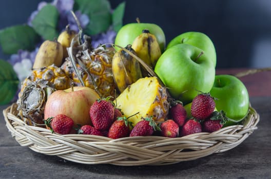 still life of mix fruits , apple with strawberry, pineapple and banana on wooden basket
