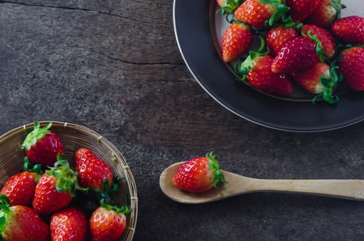 still life of fresh red strawberries  on  dish and basket with spoon  over wooden background