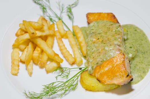roasted salmon served with green sauce and french fries  on white plate
