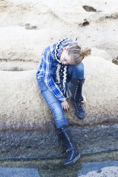 A young girl sitting alone on a cliff, looking down, lost, worried