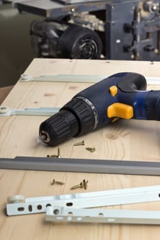 Furniture parts and electric screwdriver on a wooden table in workshop