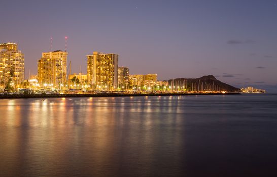 Panorama of the nightime skyline of Honolulu and Waikiki from Ala Moana park after the sun sets with lights illuminating the facades of the hotels and apartments
