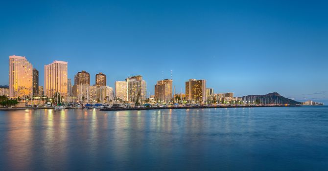 Panorama of the nightime skyline of Honolulu and Waikiki from Ala Moana park as the sun sets and illuminates the facades of the hotels and apartments