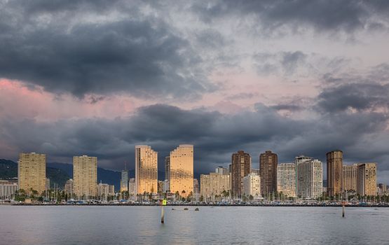 Panorama of the skyline of Honolulu and Waikiki from Ala Moana park as the sun sets and illuminates the facades of the hotels and apartments