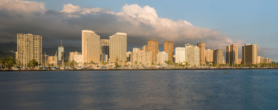 Panorama of the skyline of Honolulu and Waikiki from Ala Moana park as the sun sets and illuminates the facades of the hotels and apartments