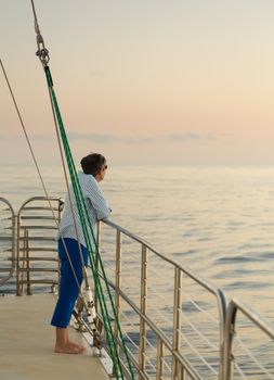 Middle aged caucasian woman on an ocean sunset cruise and leaning against the railings. Relaxed and looking at the horizon