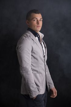 Attractive elegant young man standing with smoke around him, dark background