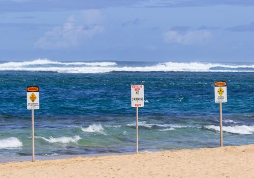 Three warning sign no swimming and strong currents in treacherous winter waters on Tunnels Beach in Kauai Hawaii