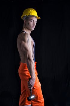 Handsome young construction worker with naked torso, wearing yellow hardhat, holding hammer