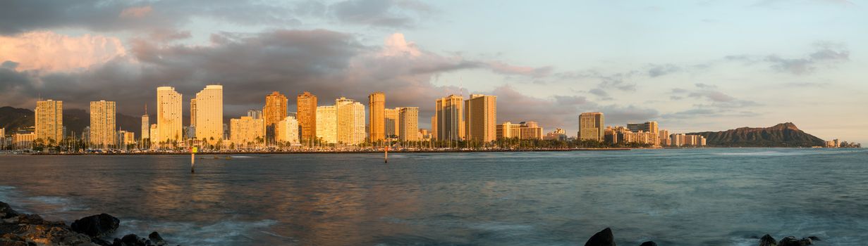 Panorama of the skyline of Honolulu and Waikiki from Ala Moana park as the sun sets and illuminates the facades of the hotels and apartments