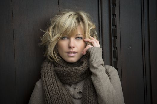 Attractive blonde young woman outside, with winter clothes against wooden door