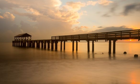 Long exposure image of Waimea pier at sunset blurs the ocean and bathes the structure in the warm glow of the setting sun. Taken on island of Kauai in Hawaiian islands