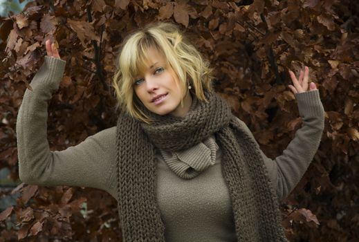 Attractive blonde young woman against autumn leaves wearing wool clothes