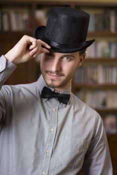 Attractive young man wearing top hat and bow tie, looking at camera. Indoors shot